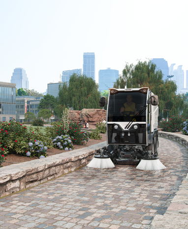 Eine CityCat VR17e Kehrmaschine von Bucher kehrt einen Gehweg in einem Park.