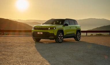 Ein grüner Jeep Compass steht bei Sonnenuntergang in einer Berglandschaft.