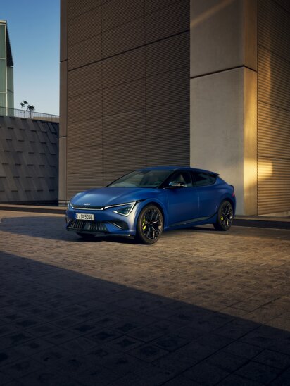 Blauer Kia EV6 parkt vor moderner Architektur, seitlich von vorne fotografiert. | © Kia Europe GmbH