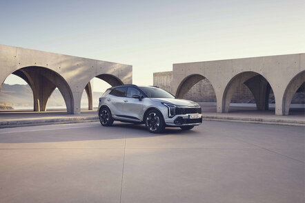 Grauer Kia Sportage in schräger Frontansicht steht vor moderner Architektur.