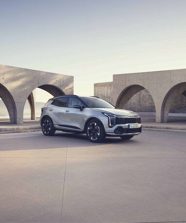 Grauer Kia Sportage in schräger Frontansicht steht vor moderner Architektur.