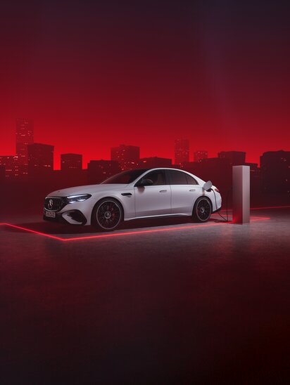 Eine weiße Mercedes-AMG E-Klasse Limousine wird nachts in einer futuristischen Stadtumgebung aufgeladen. | © Mercedes-Benz Group AG