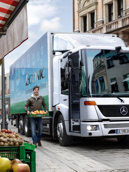 Ein Mercedes-Benz Econic Lkw liefert Obst an einen Marktstand.