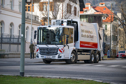 Ein weißer Mercedes-Benz eEconic Müllwagen fährt durch eine städtische Umgebung. Aufschrift: "Voll elektrisch durch die Stadt".