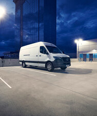 Ein weißer Mercedes-Benz eSprinter Kastenwagen steht nachts auf einem Parkplatz und ist an einer E-Tankstelle angeschlossen.  | © Mercedes-Benz AG
