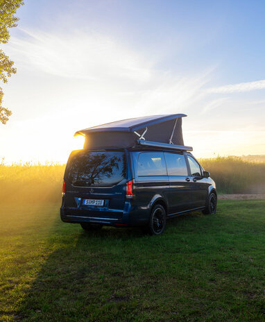 Ein blauer Mercedes-Benz Marco Polo mit Aufstelldach parkt auf einer Wiese am Ufer eines Sees im Morgenlicht. | © Mercedes-Benz Österreich