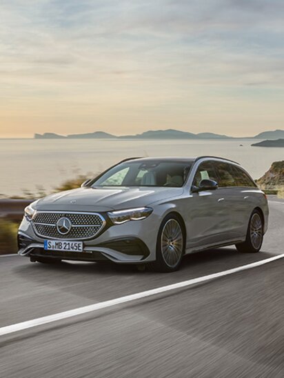 Silbernes Mercedes-Benz E-Klasse T-Modell fährt entlang einer Küstenstraße mit Meereshintergrund.