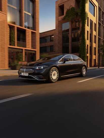 Ein schwarzer Mercedes-Benz EQS fährt durch eine Stadtstraße vor modernen Backsteingebäuden. | © Mercedes-Benz AG