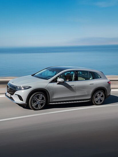 Ein silberner Mercedes-Benz EQS SUV fährt auf einer Küstenstraße.