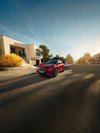 Ein roter Mercedes-Benz GLA parkt auf einer sonnigen Straße vor einem modernen Gebäude. | © Mercedes-Benz