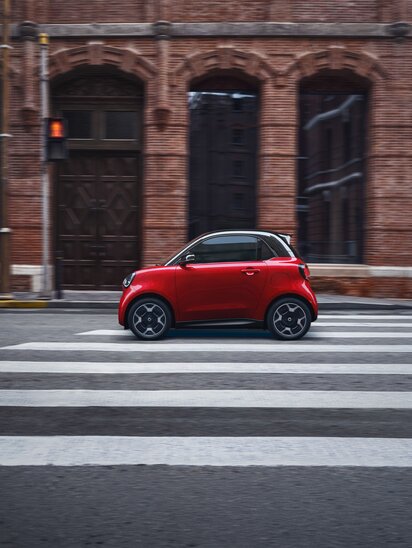 Roter smart #2 auf einem Zebrastreifen vor Backsteingebäude.